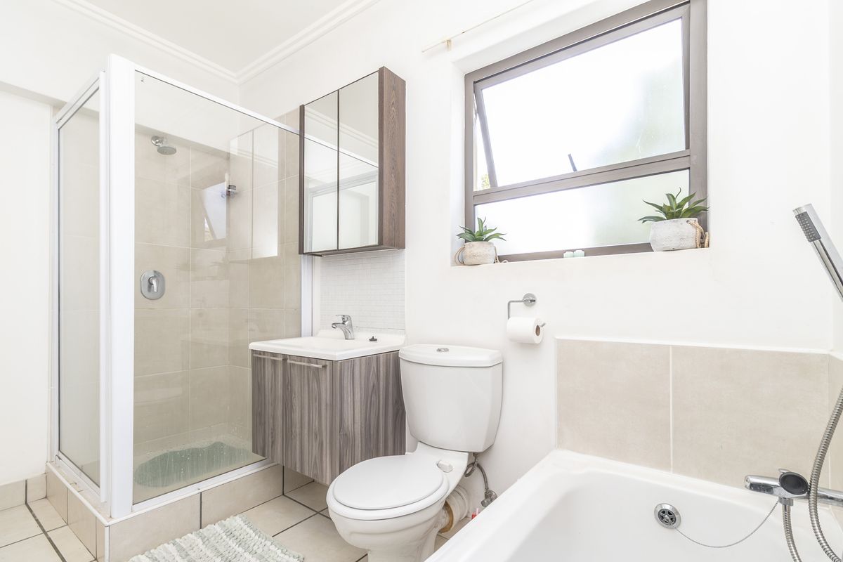 A well-maintained bathroom featuring a glass shower enclosure, a modern vanity with basin, a toilet, and a bathtub with tiled finishes.