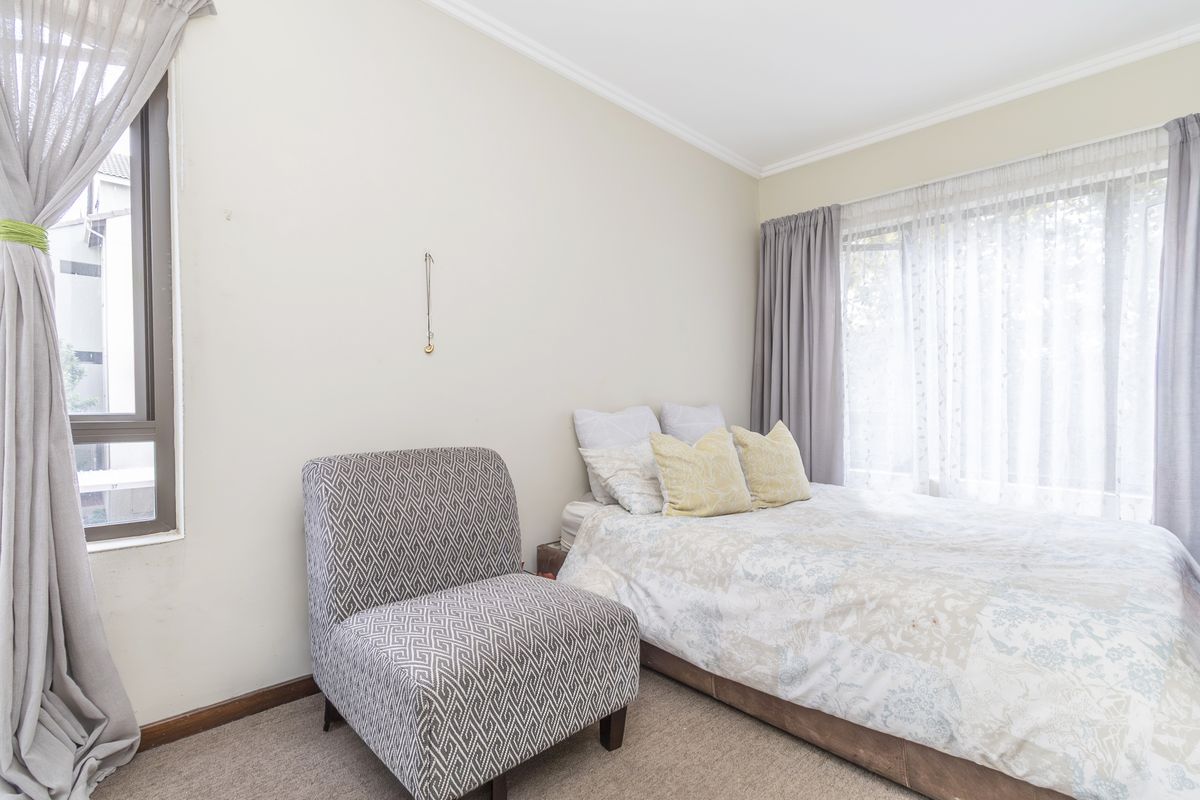 A bright bedroom featuring neutral walls, carpeted flooring, and large windows with curtain tracks, offering a comfortable and well-lit living space.