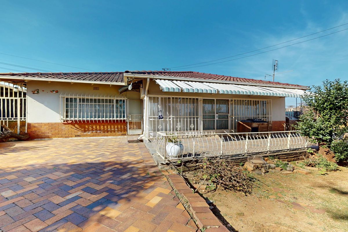 Rear exterior view of the house featuring a paved patio area, retractable awning, and security bars on windows and doors.