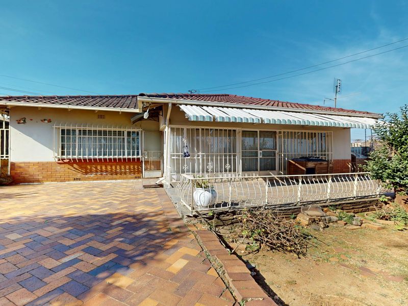 Rear exterior view of the house featuring a paved patio area, retractable awning, and security bars on windows and doors.