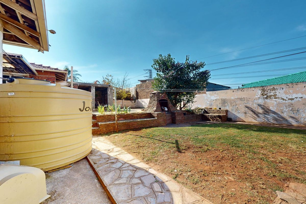 Rear garden area featuring a brick built-in braai, stone paved pathway, and a large water storage tank against a weathered boundary wall.