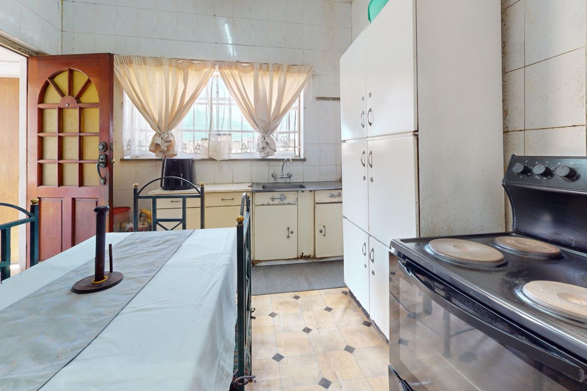 A dated kitchen featuring original cabinetry, tiled splashbacks, and a freestanding electric stove, requiring significant modernization and renovation to improve functionality and aesthetic appeal.