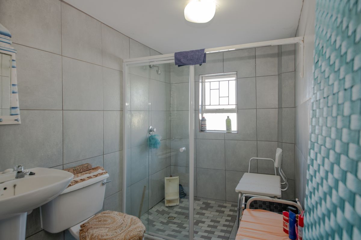 A functional bathroom featuring a pedestal basin, toilet, and a glass-enclosed shower with tiled finishes throughout.