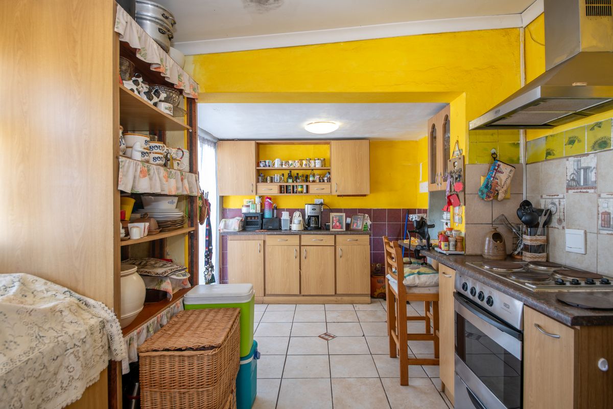 A dated kitchen featuring wood-look cabinetry, tiled flooring, and a built-in stove, requiring cosmetic updates to modernize the space.