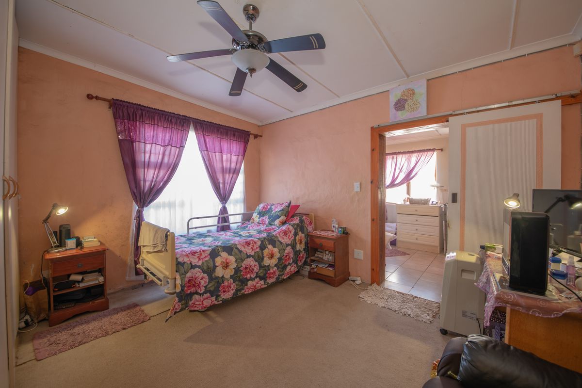 A bedroom featuring a ceiling fan, built-in cupboard, and sliding door access to an adjacent room, with visible wear to the wall finishes.