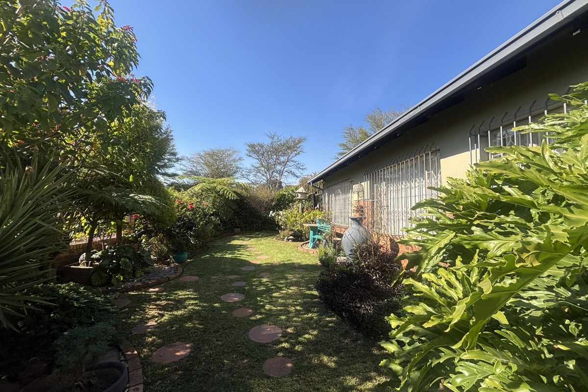 A private rear garden featuring a lawn, established landscaping, and a paved pathway alongside the townhouse exterior with security bars on windows.