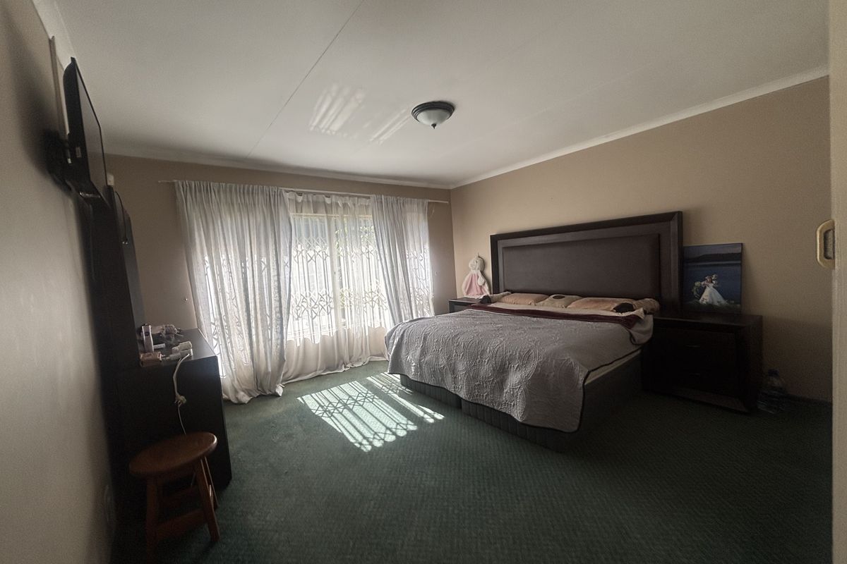 Spacious bedroom featuring wall-to-wall carpeting, large window with curtain tracks, and a central ceiling light fixture.