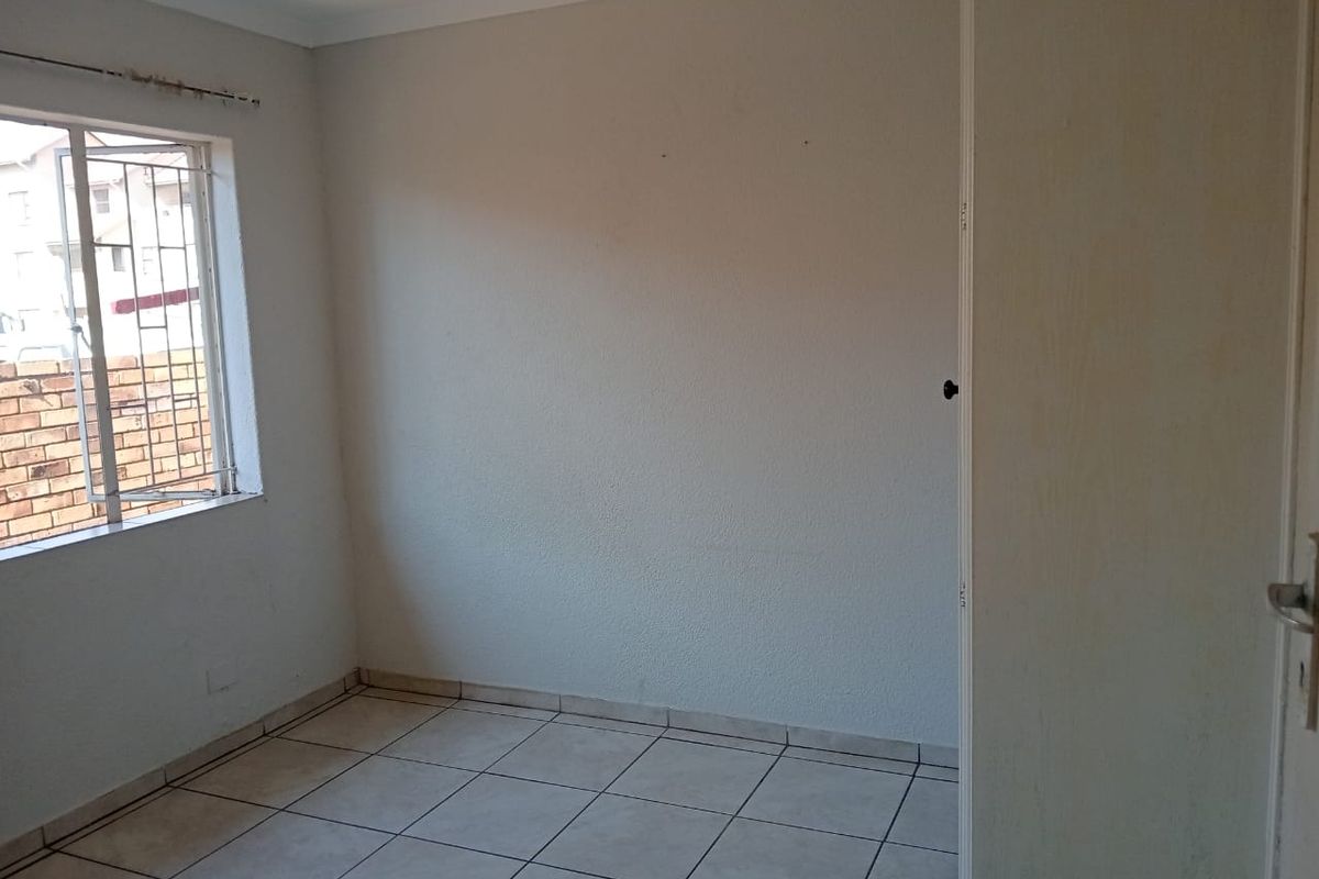 An empty bedroom featuring tiled flooring, a built-in cupboard, and a window fitted with security bars.