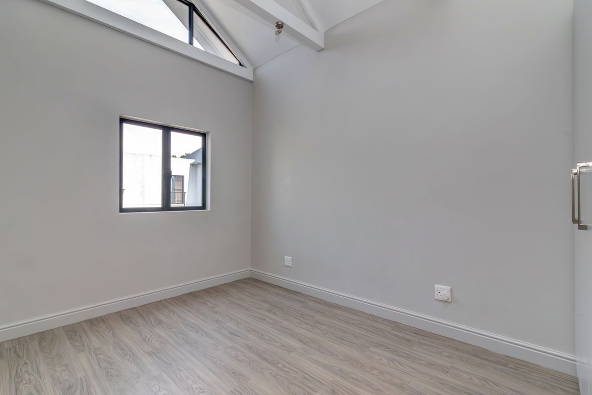 A bright, empty bedroom featuring high vaulted ceilings, modern laminate flooring, and a large window allowing for ample natural light.