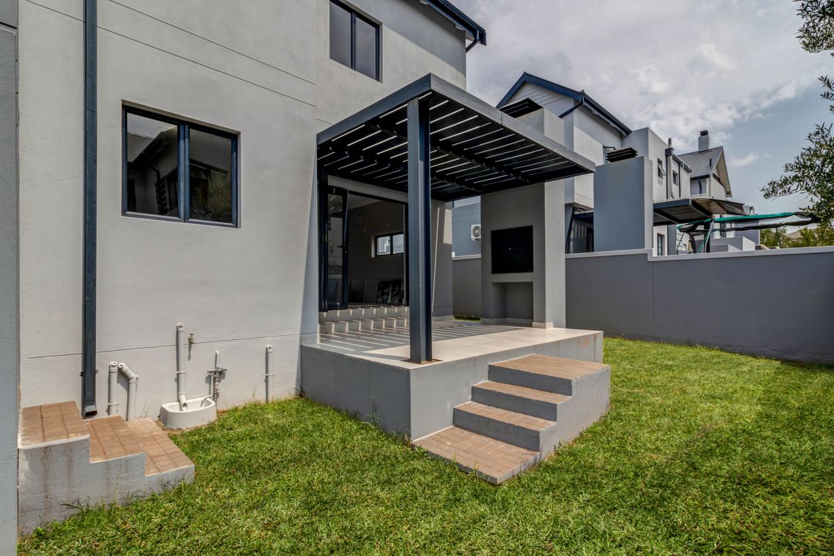 Rear view of the property featuring a covered patio with a built-in braai, concrete steps, and a landscaped garden area.