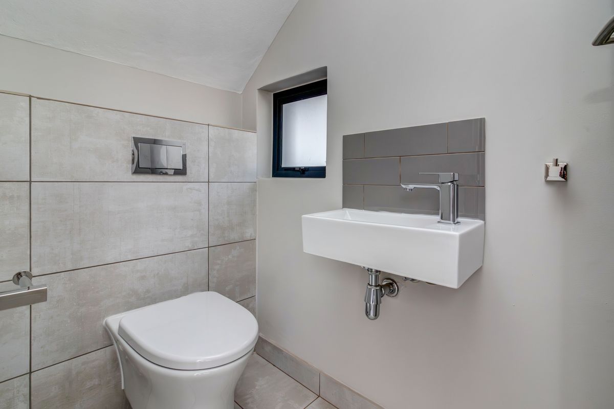 A modern guest cloakroom featuring a wall-mounted basin, concealed cistern toilet, and neutral tiled finishes.