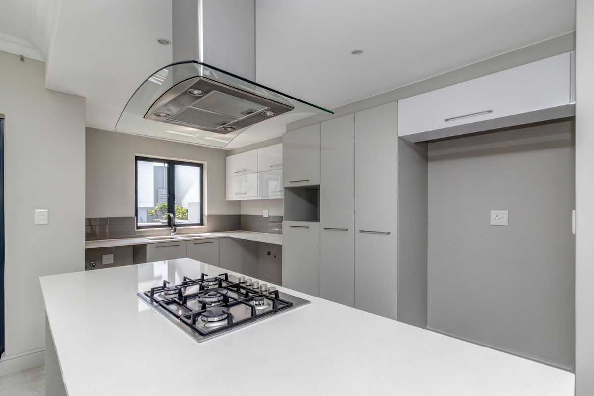 Modern kitchen featuring a central island with a built-in gas hob, sleek cabinetry, stone countertops, and a stainless steel extractor fan.