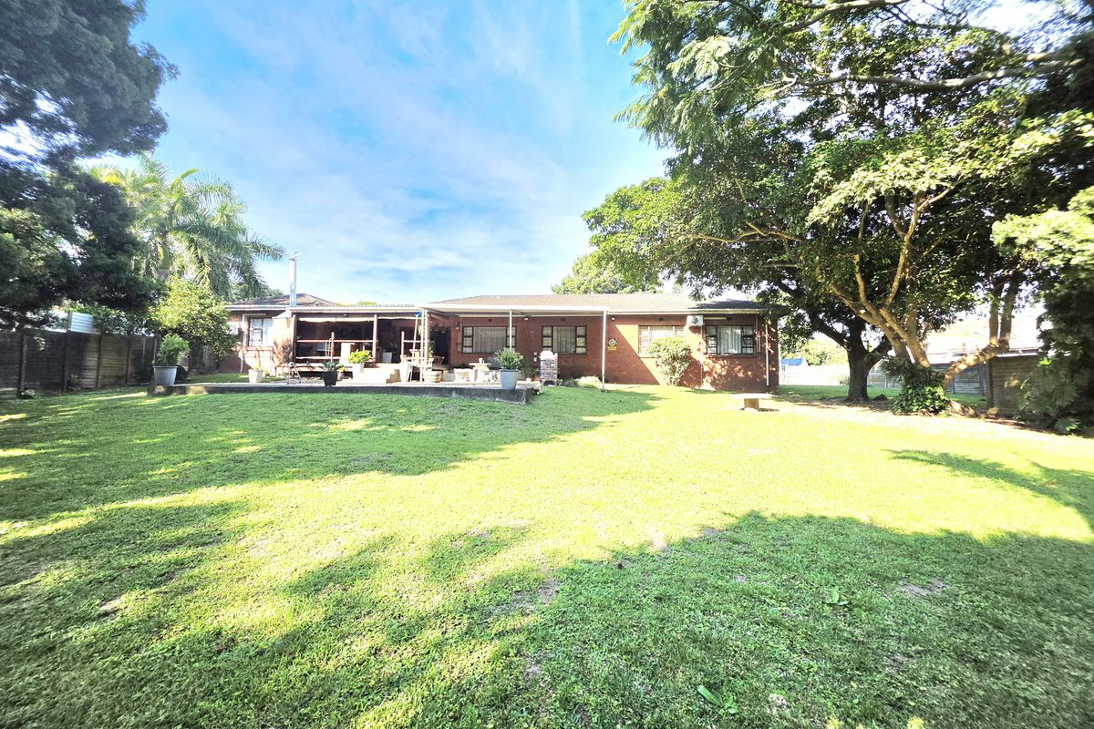 A spacious rear garden featuring a brick-built house with a covered patio area, mature trees, and a well-maintained lawn.