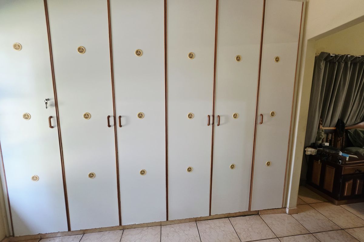 A bedroom featuring extensive floor-to-ceiling built-in cupboards with a classic design and neutral tiled flooring.