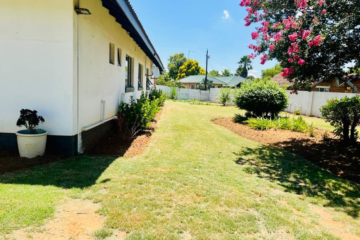 A well-maintained rear garden featuring a lawn, established trees, and a perimeter wall along the side of the house.