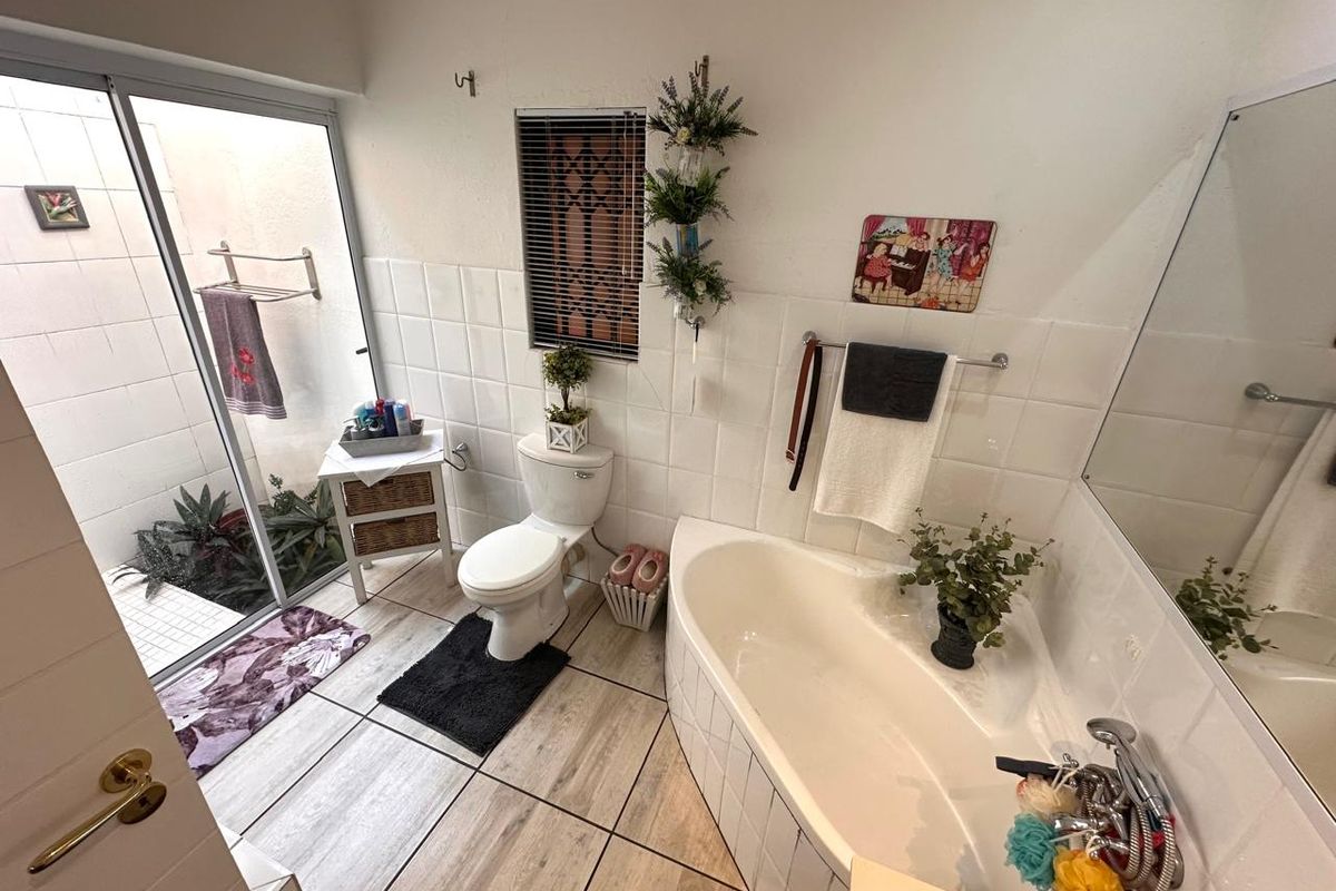 A functional bathroom featuring a corner bathtub, toilet, and tiled finishes, with a sliding glass door providing access to a small outdoor area.