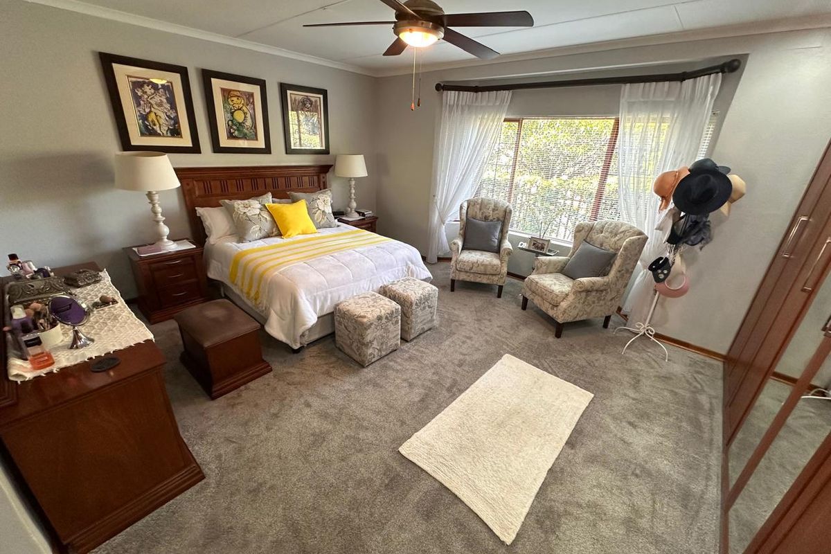 A spacious, well-maintained bedroom featuring neutral wall tones, plush carpeting, a ceiling fan, and a large built-in wardrobe for ample storage.