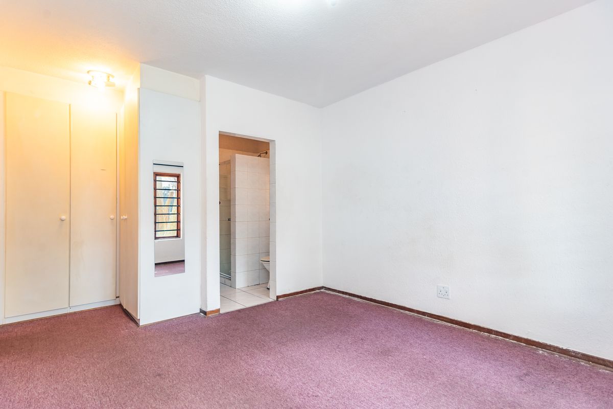 An empty bedroom featuring built-in cupboards, carpeted flooring, and direct access to an en-suite bathroom.
