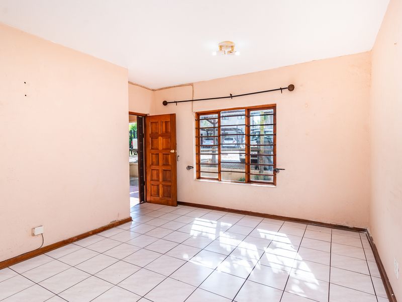 An empty living room featuring tiled flooring, a wooden window with security bars, and a wooden entrance door.