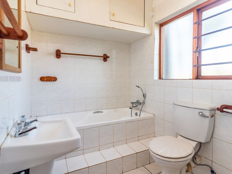 A functional bathroom featuring a built-in bathtub, pedestal basin, toilet, and tiled finishes, offering a blank canvas for modern renovation.