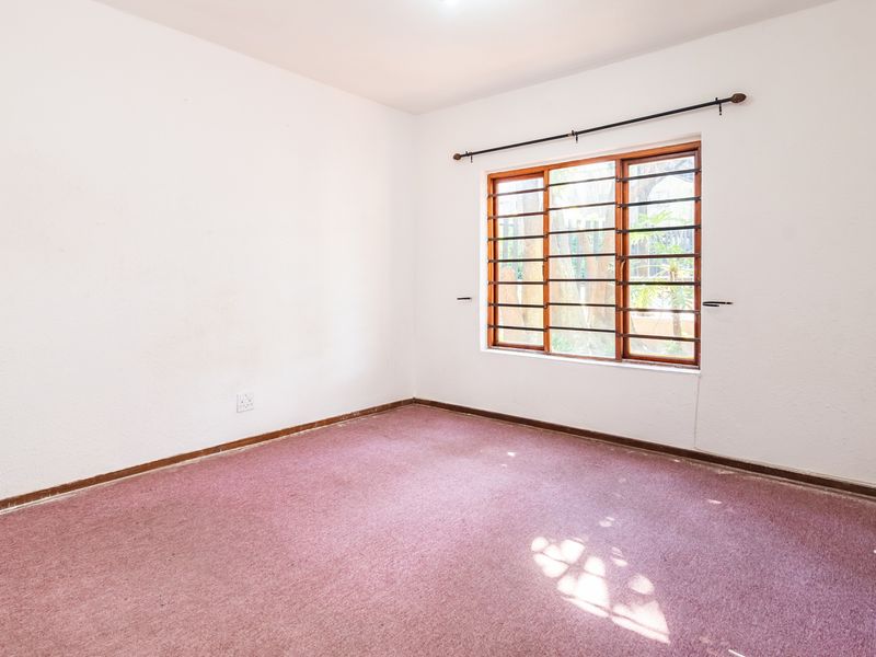 An empty bedroom featuring carpet flooring and a wooden window frame with security bars.