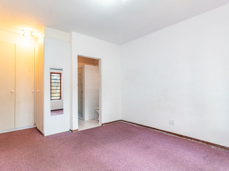 An empty bedroom featuring built-in cupboards, carpeted flooring, and direct access to an en-suite bathroom.