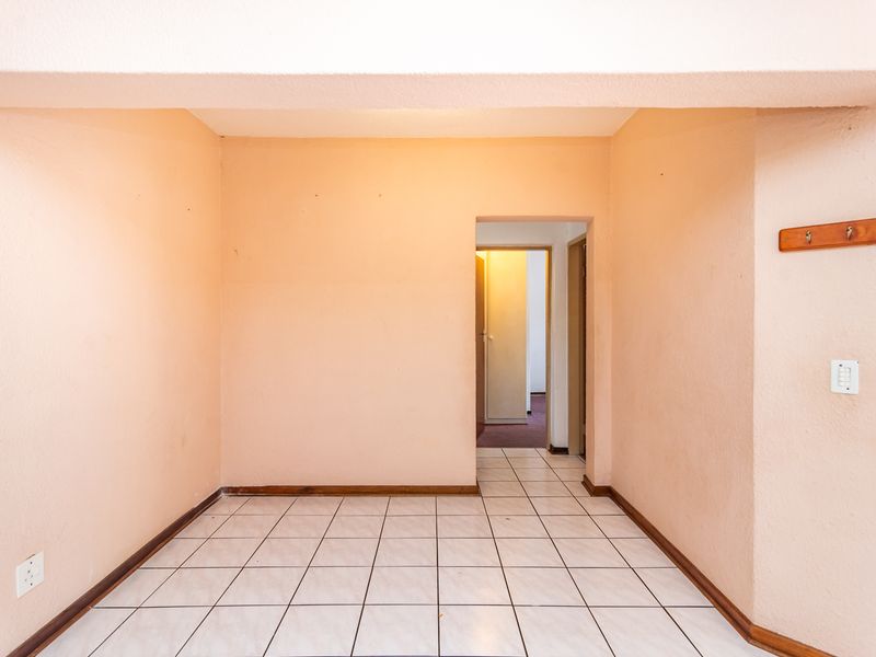 An empty, tiled hallway featuring neutral peach-toned walls, skirting boards, and a wall-mounted coat rack, leading into an adjacent room.