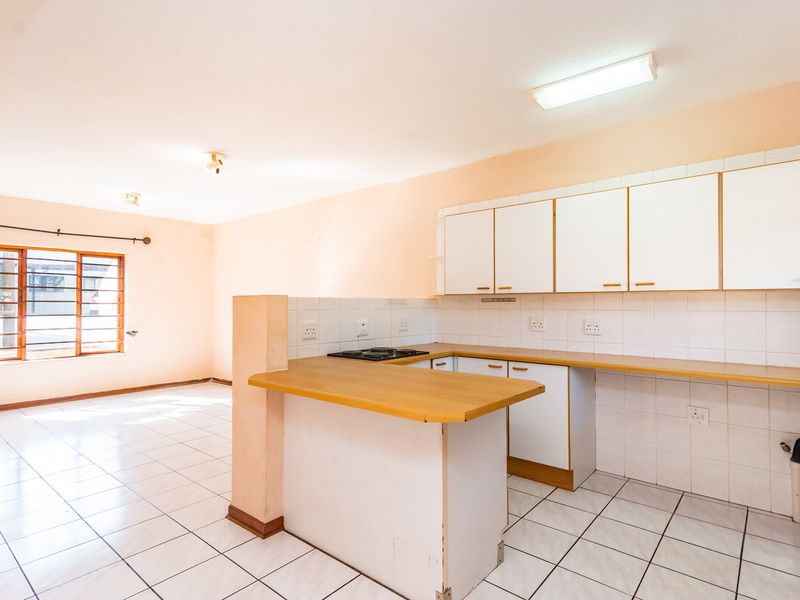 An open-plan kitchen and living area featuring tiled flooring, built-in cabinetry, a breakfast bar, and a hob, offering a blank canvas for renovation.