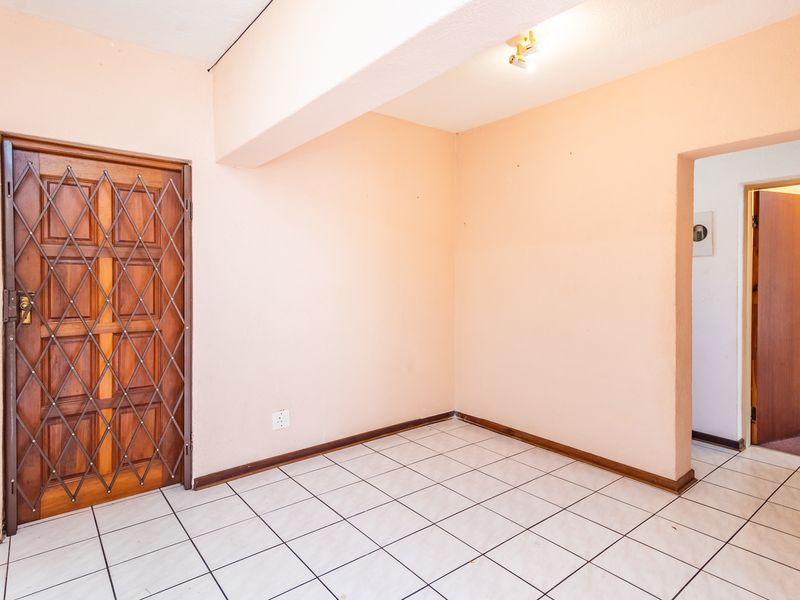 An empty entrance area featuring tiled flooring, a wooden door with a security gate, and access to an adjacent room.