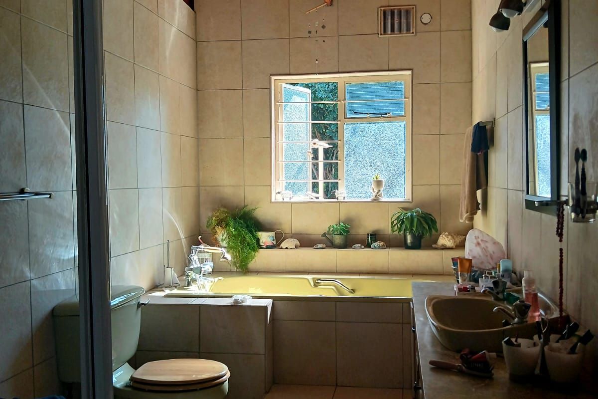 A dated bathroom featuring a built-in bathtub, tiled walls, a wooden ceiling, and a vanity unit with a basin.