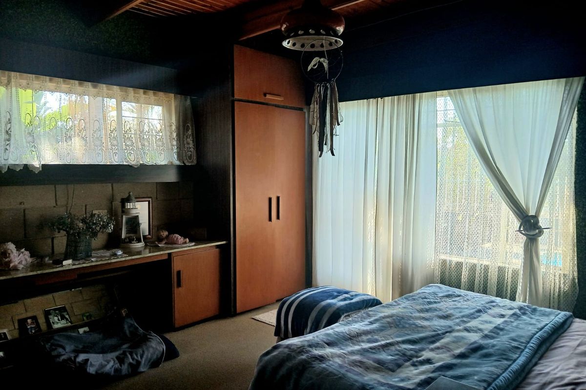 A bedroom featuring built-in wooden cabinetry, exposed timber ceiling beams, and large windows allowing natural light.