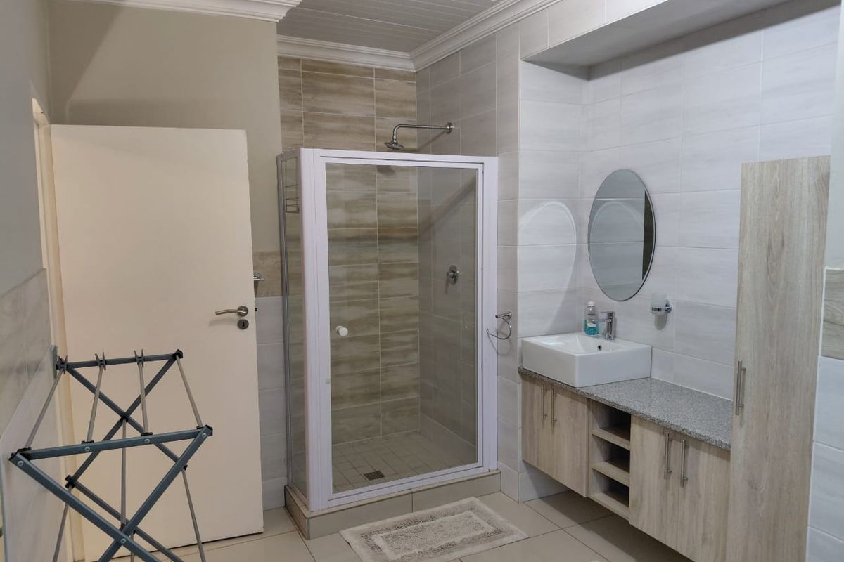 Modern bathroom featuring a glass shower enclosure, a contemporary vessel sink with vanity storage, and neutral wall and floor tiling.