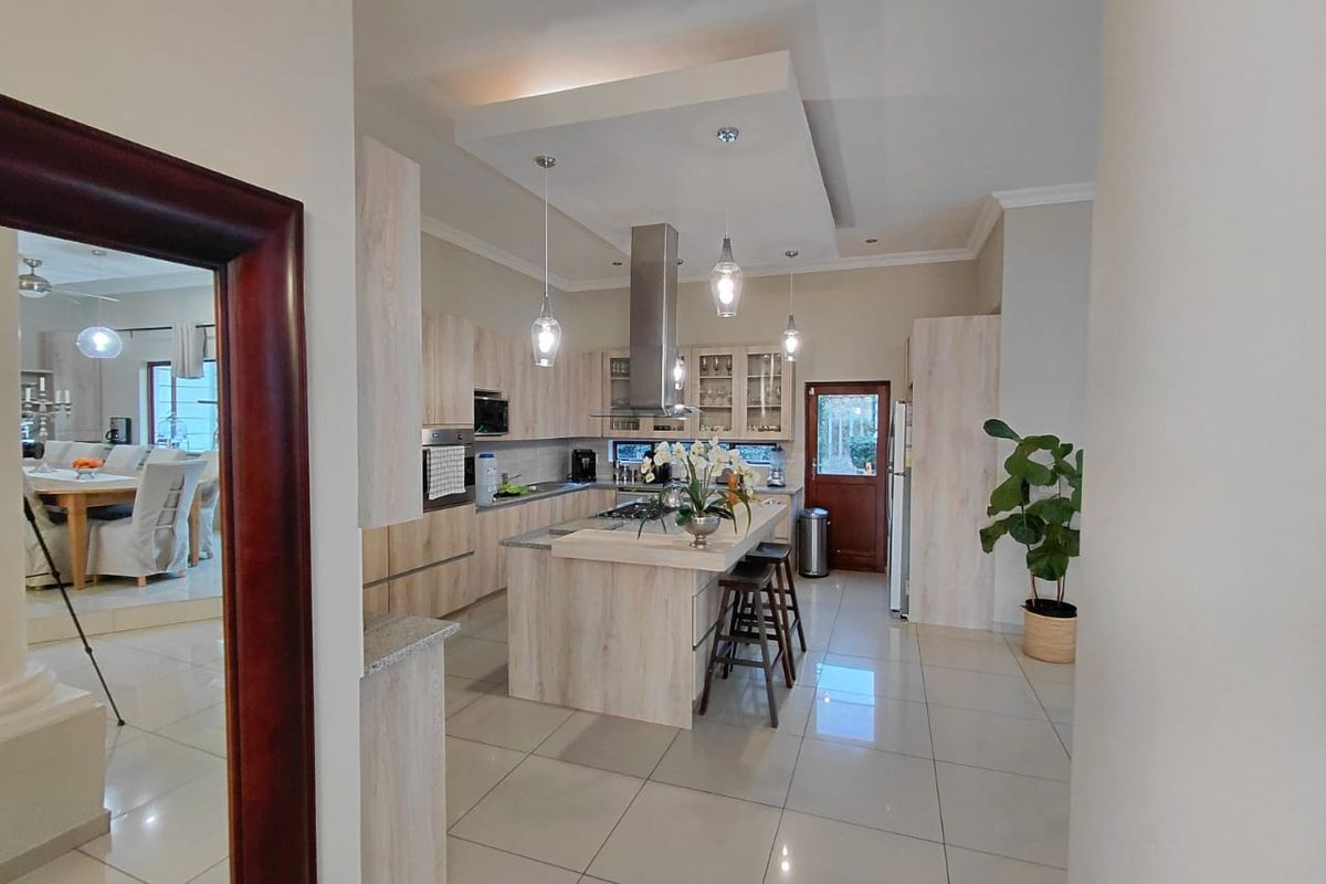Modern kitchen featuring light wood cabinetry, a central island with stone countertops, stainless steel extractor fan, and integrated appliances, opening into a dining area.