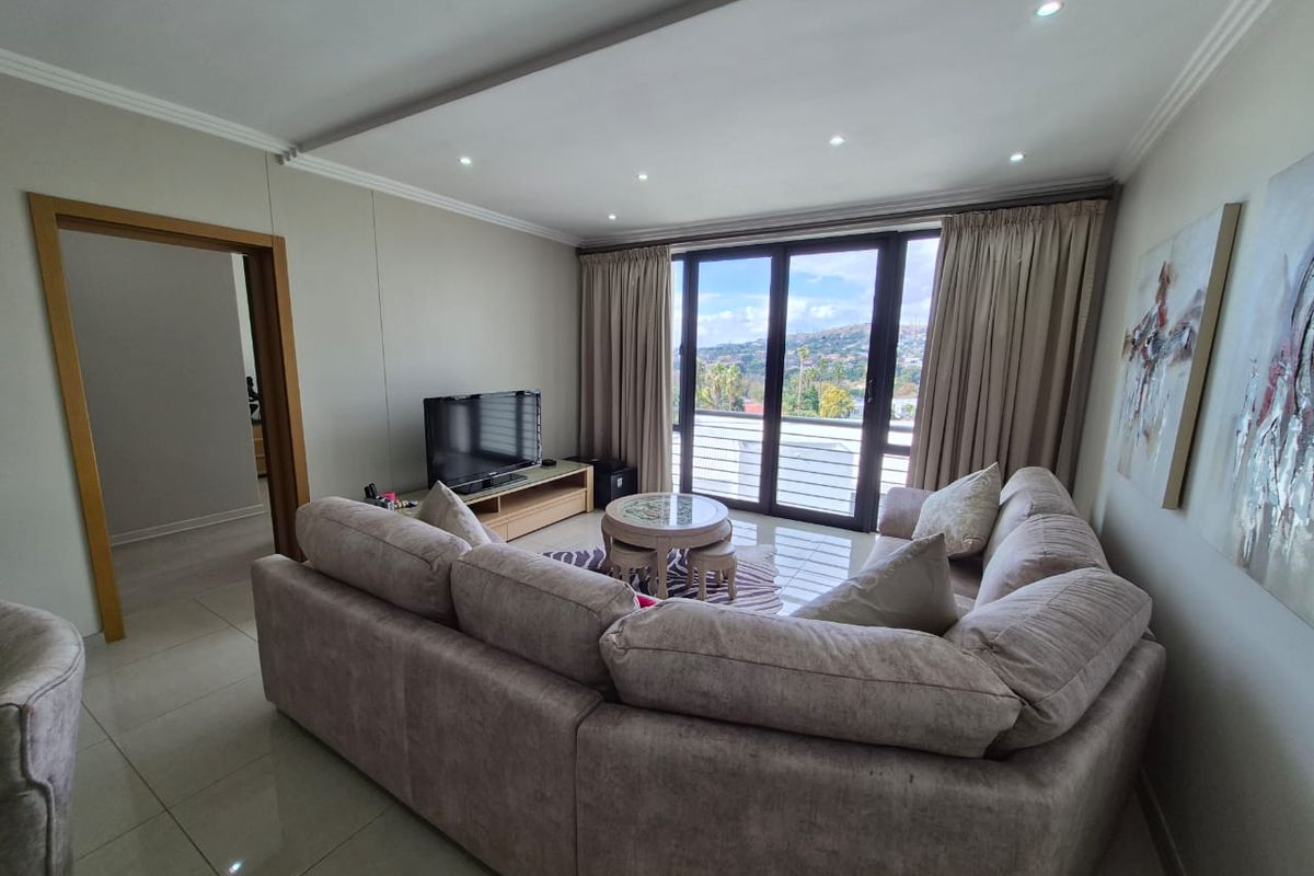 A well-maintained living room featuring tiled floors, recessed ceiling lighting, and large sliding glass doors that open to a balcony with scenic views.