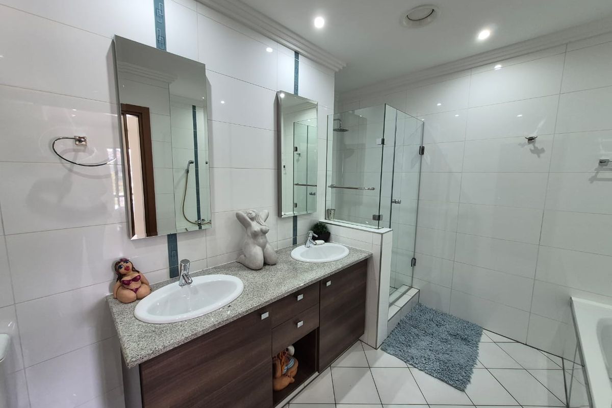 Modern bathroom featuring a double vanity with granite countertops, glass-enclosed shower, and clean white wall tiling.