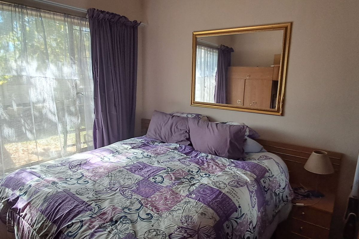 A standard bedroom featuring a built-in headboard and large window with curtain rails, providing natural light and a view of the exterior.