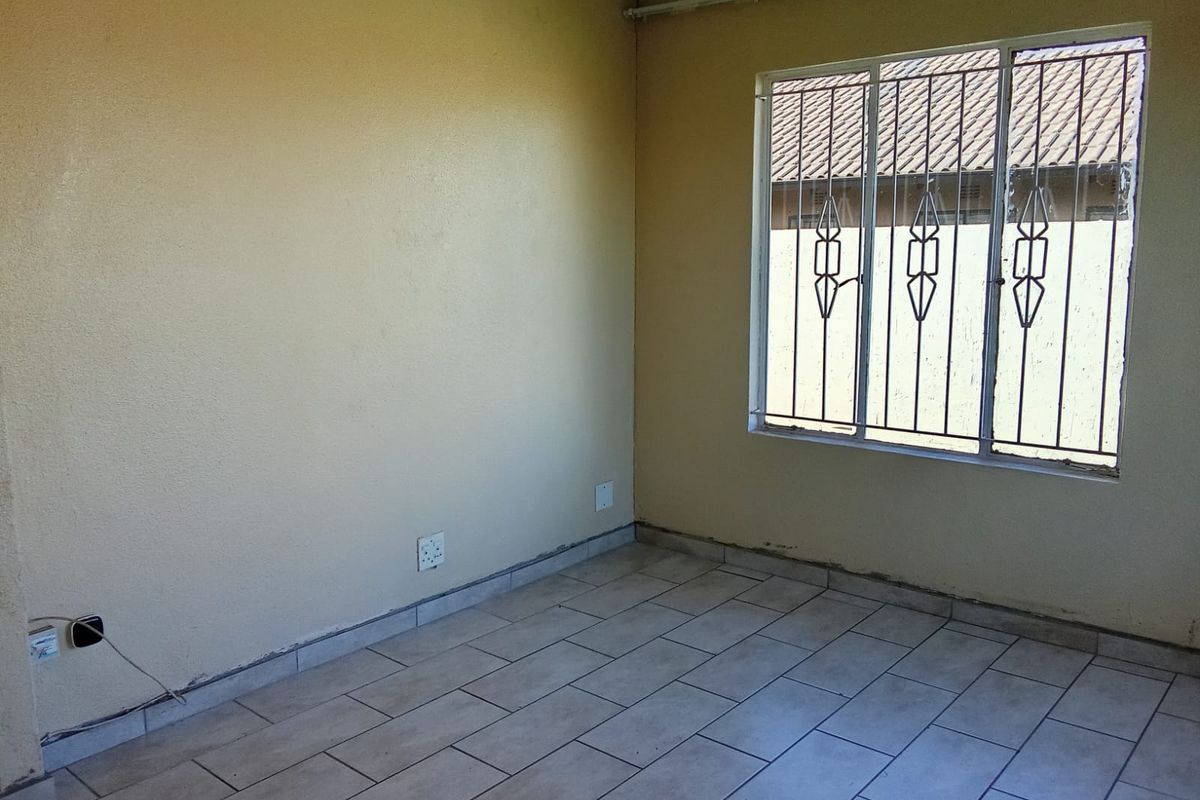 An empty bedroom featuring tiled flooring, security bars on the window, and basic electrical fixtures, requiring minor cosmetic finishing and paint updates.