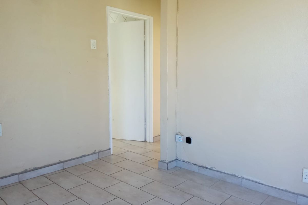 An empty living area featuring neutral wall paint and ceramic floor tiles, providing a blank canvas for potential interior design updates.