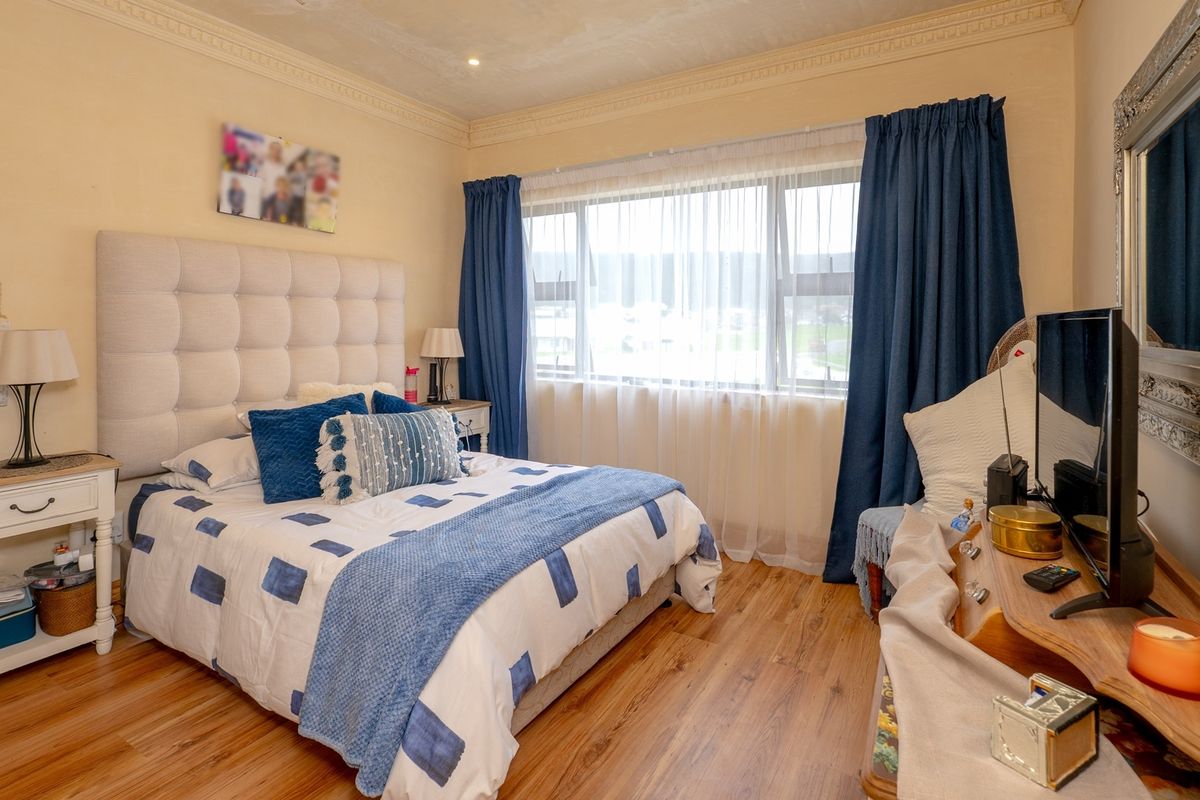 A well-maintained bedroom featuring laminate flooring, crown molding, and a large window with natural light.
