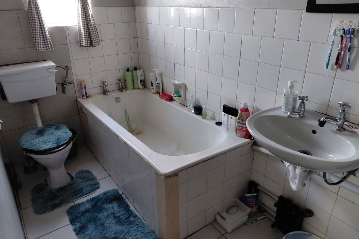 A dated bathroom featuring a standard bathtub, pedestal basin, and toilet with white wall tiling and floor tiles.