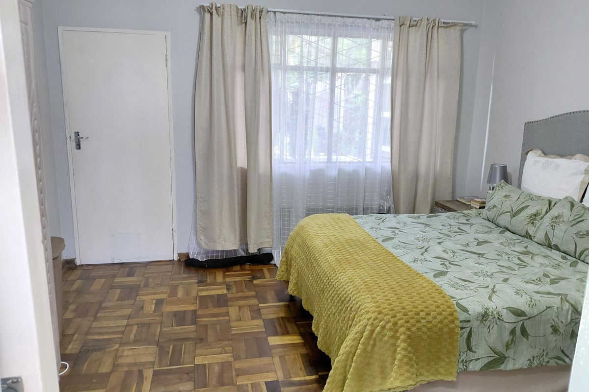 A bedroom featuring classic parquet flooring and a window fitted with security bars, offering a functional and well-lit living space.
