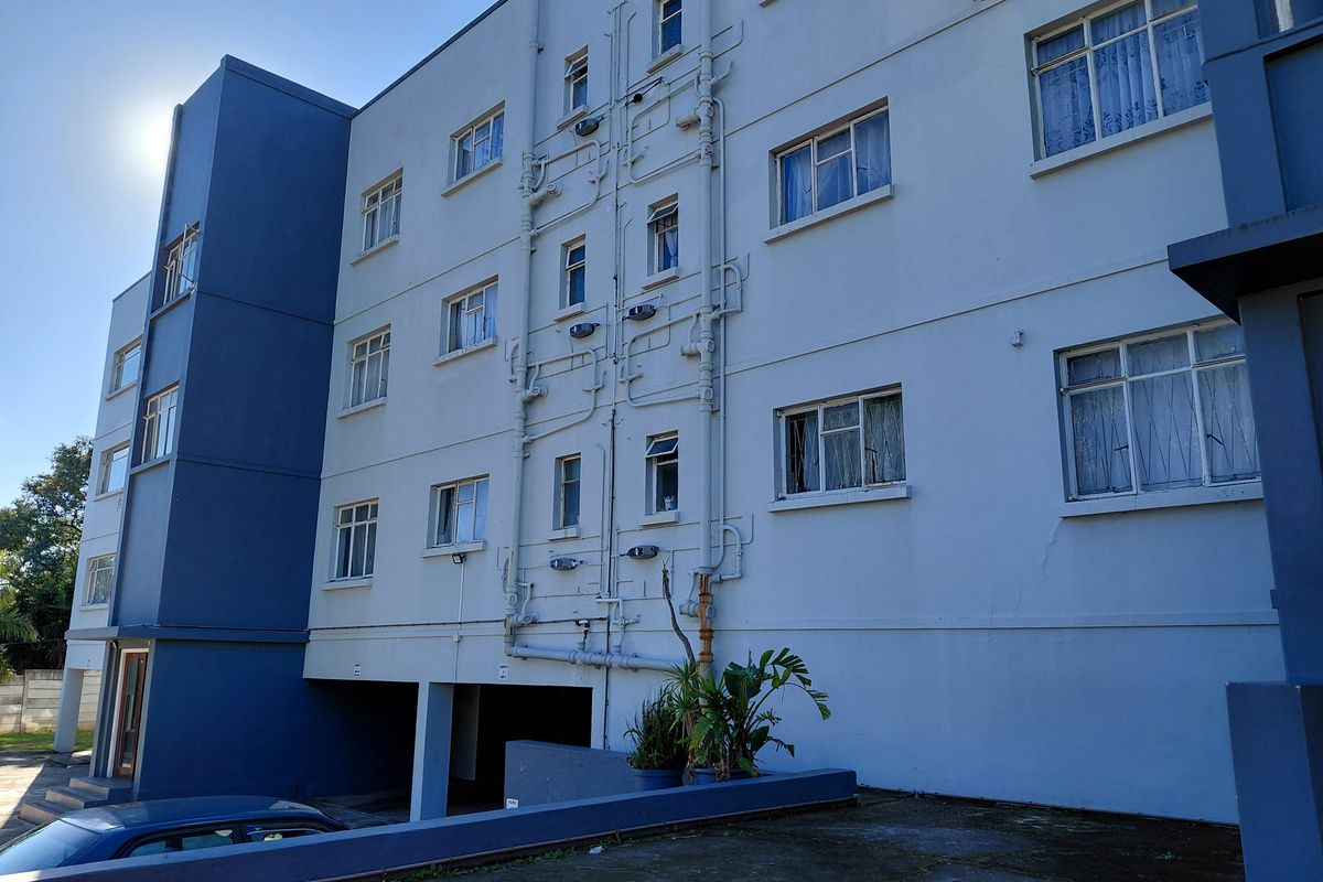 Rear elevation of a multi-story townhouse complex featuring exposed plumbing, casement windows, and a ground-level covered parking area.