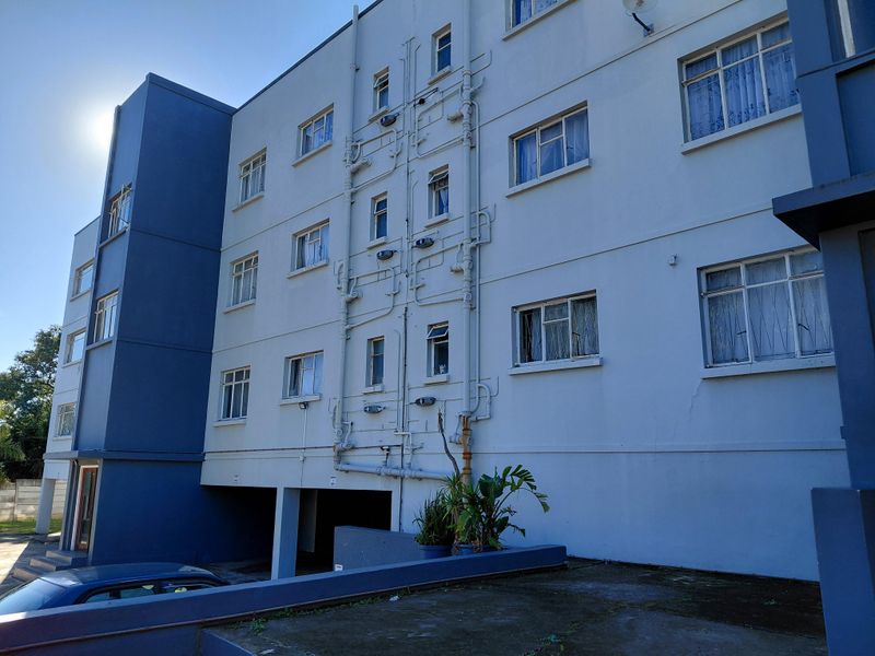 Rear elevation of a multi-story townhouse complex featuring exposed plumbing, casement windows, and a ground-level covered parking area.