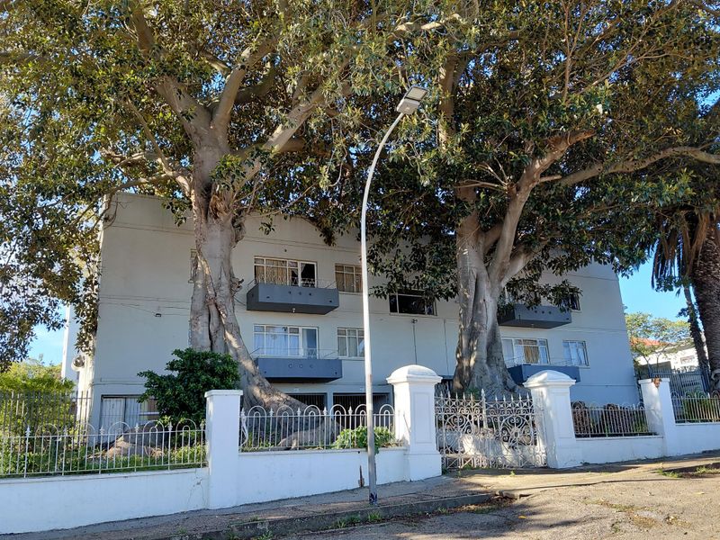 Front elevation of a townhouse complex featuring mature trees, wrought iron fencing, and private balconies.