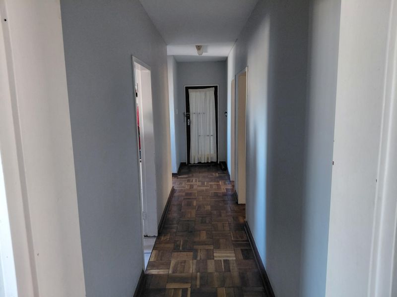 A clean, empty hallway featuring classic parquet flooring and neutral wall finishes, providing access to multiple rooms within the townhouse.