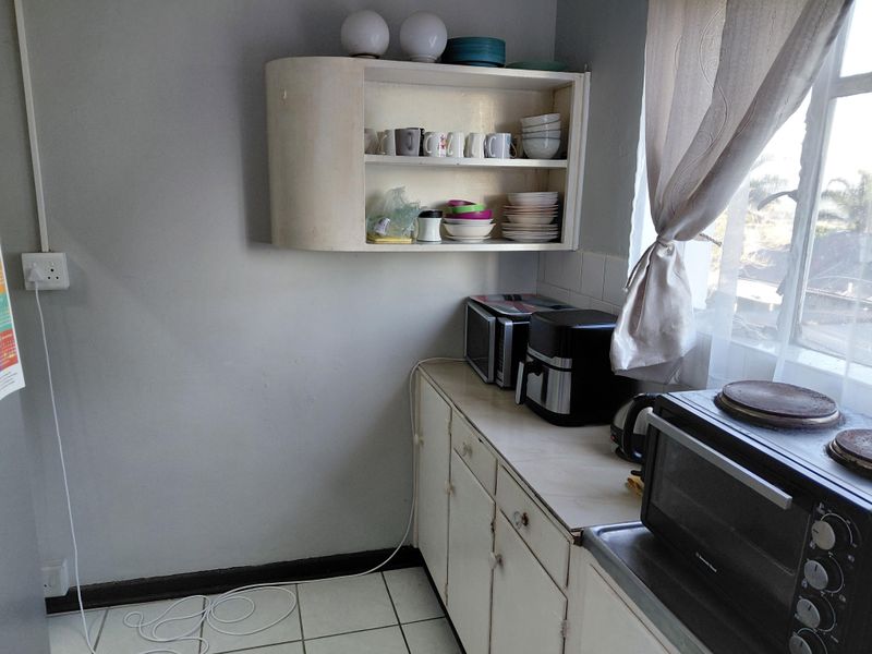A compact kitchen area featuring dated built-in cabinetry, tiled flooring, and wall-mounted shelving, offering potential for a modern renovation.