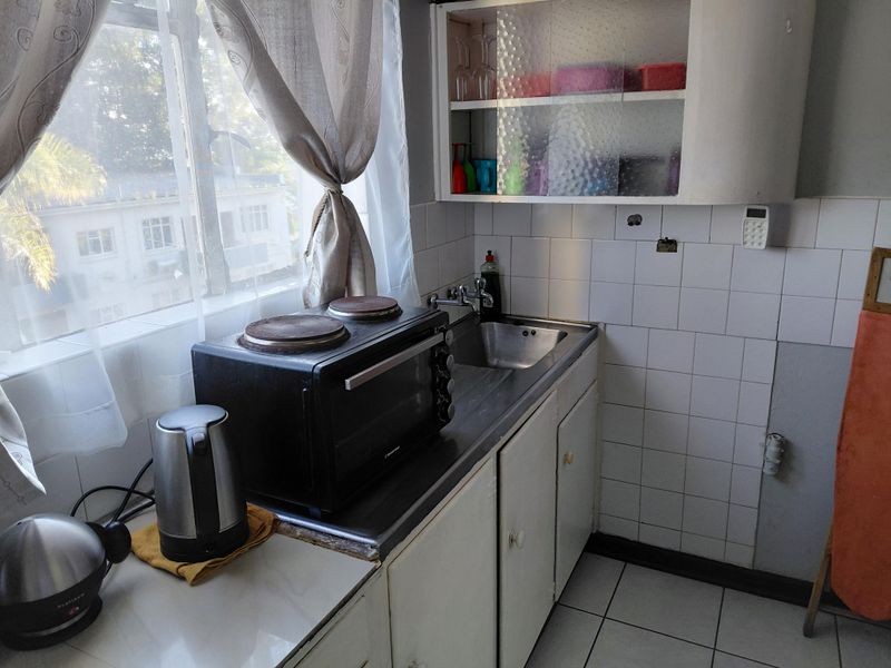 A compact kitchen featuring a stainless steel sink, tiled backsplash, and built-in cabinetry, requiring some maintenance and cosmetic updates.