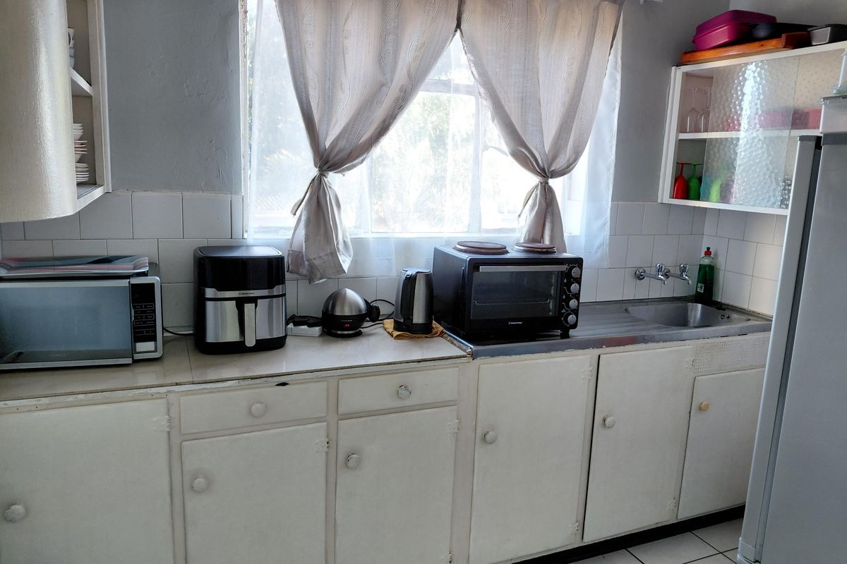 A functional kitchen featuring white built-in cabinetry, a stainless steel sink, tiled backsplash, and tiled flooring, offering potential for modernization.