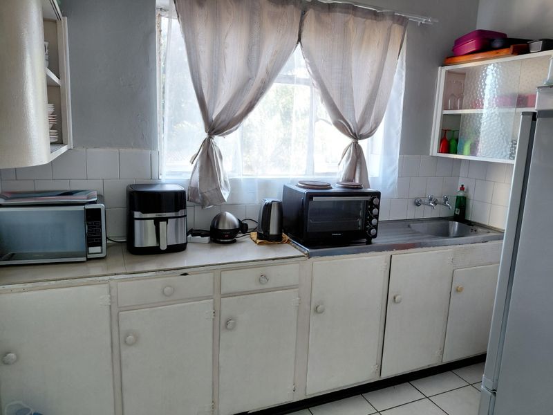 A functional kitchen featuring white built-in cabinetry, a stainless steel sink, tiled backsplash, and tiled flooring, offering potential for modernization.
