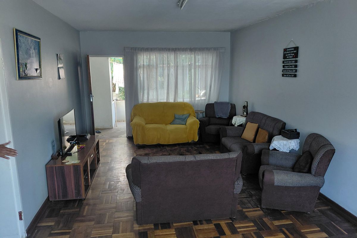 A living room featuring traditional parquet flooring and natural light through a large window, offering a functional space with potential for modern updates.